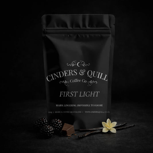 Black coffee bag labeled 'Cinders & Quill Coffee Co' with decorative elements on a dark background.