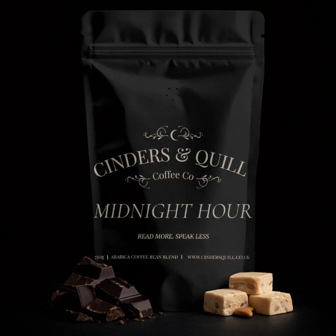 Black coffee packaging labeled 'Cinders & Quill Coffee Co. Midnight Hour' with chocolate and cookies on a black background.